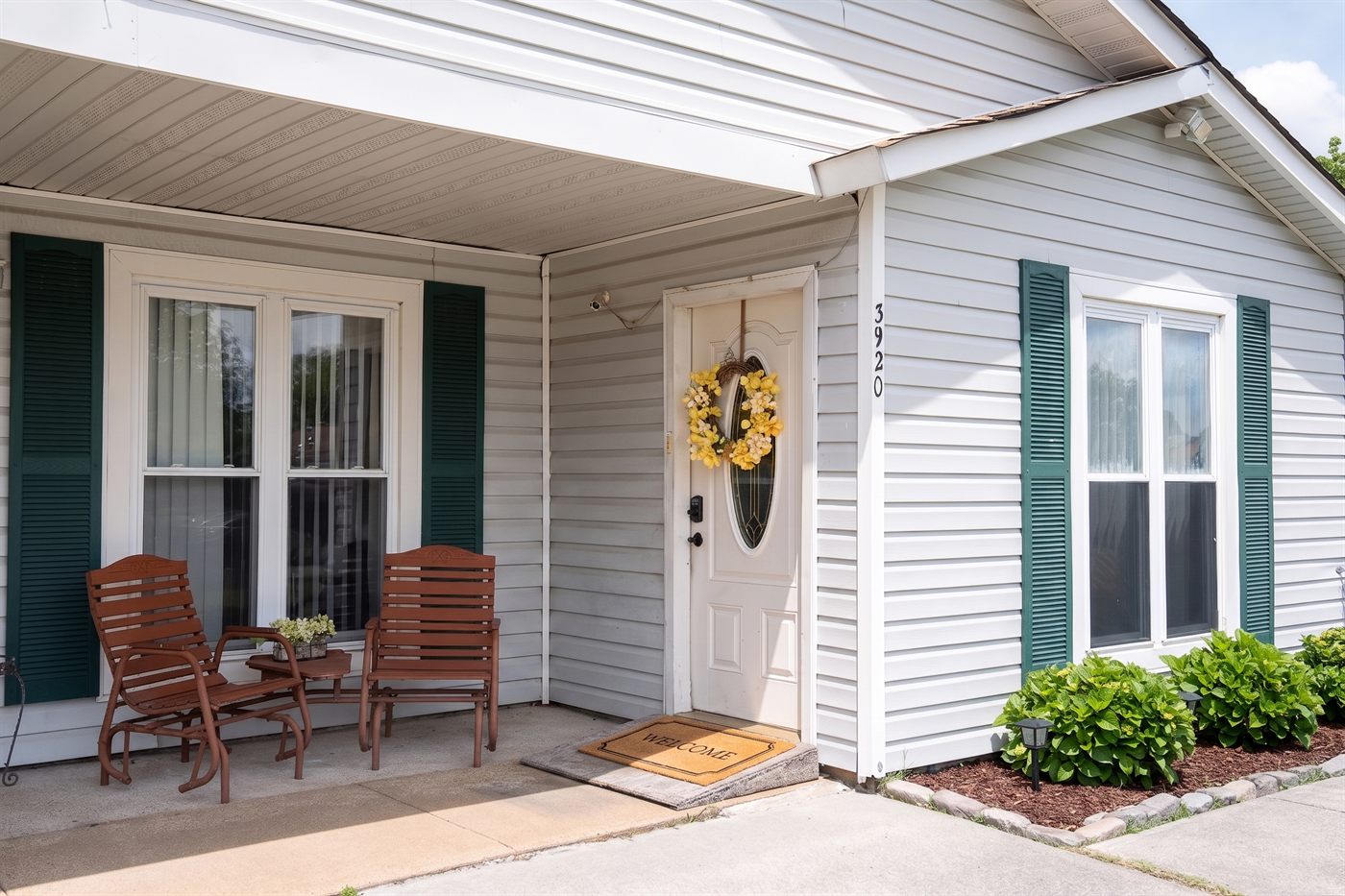 The welcoming front porch of Comfort Living at 3920 Sunstream Pkwy, Virginia Beach — two wood porch chairs, yellow welcome wreath on the door, and a Welcome doormat